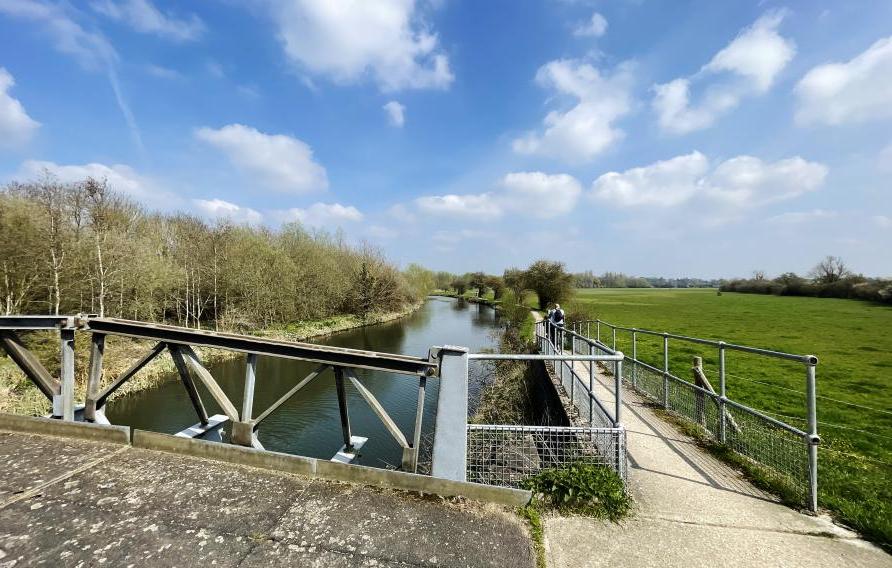 Riverbank and bridge beside a field.